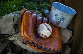 brown leather baseball mitt with baseball beside gray container and brown textile at daytime